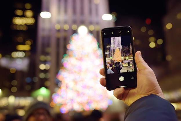 A person takes a shot on a smartphone of a famous huge live Christmas tree near Rockefeller Center
