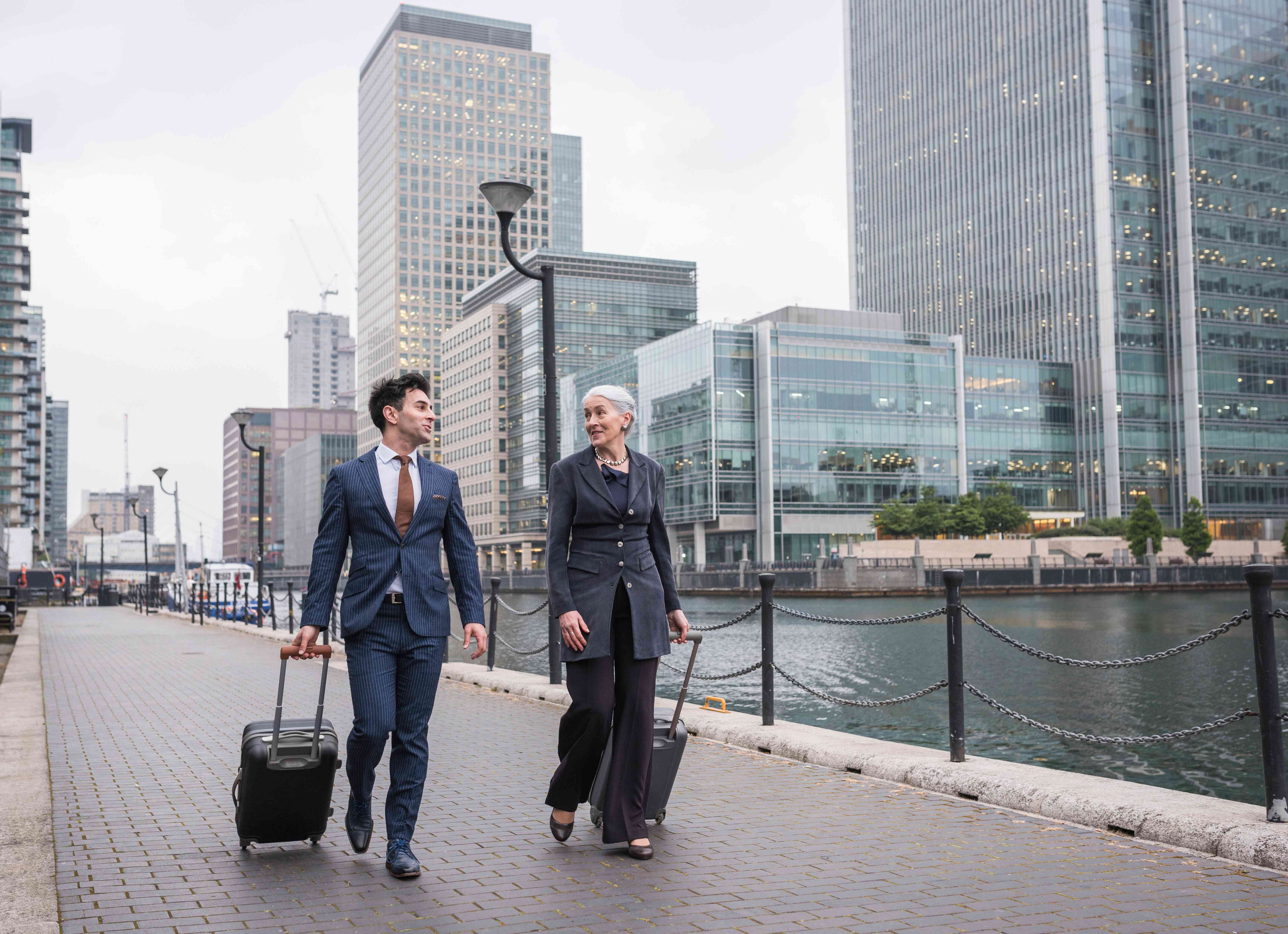 Businessman and businesswoman pulling trolley luggage, Canary Wharf, London, UK